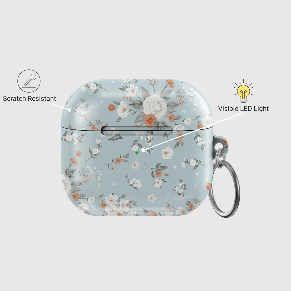 Stylish blue AirPods case with delicate peach and white floral print, featuring a glossy finish and silver keychain ring. A soft, music-inspired accessory for AirPods Pro and AirPods 3.