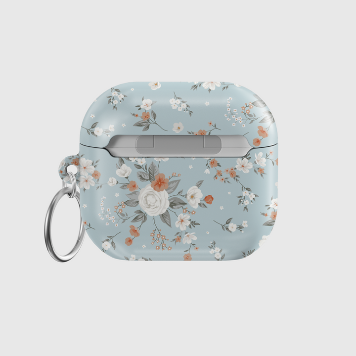 Stylish blue AirPods case with delicate peach and white floral print, featuring a glossy finish and silver keychain ring. A soft, music-inspired accessory for AirPods Pro and AirPods 3.