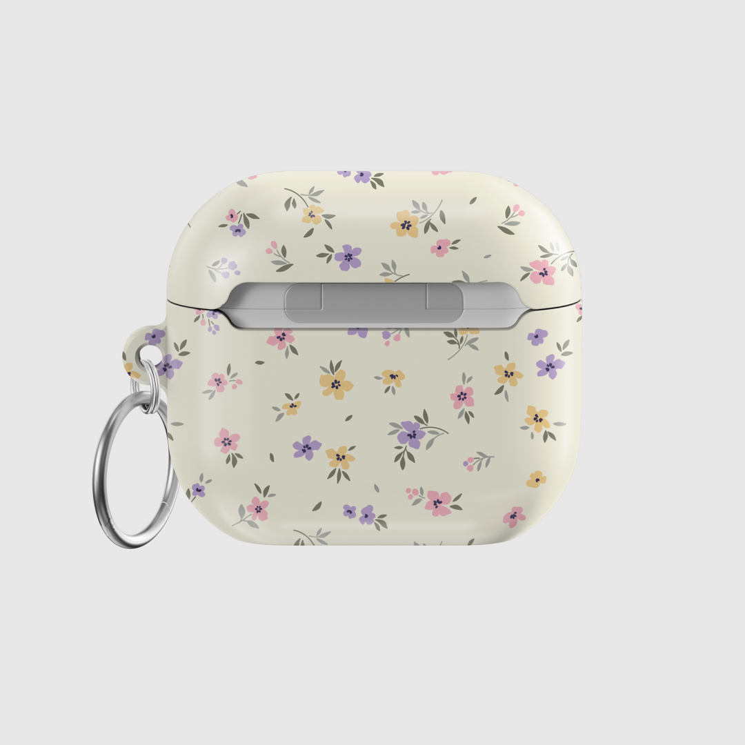 AirPods case with a cream background and tiny pastel floral print in lavender, yellow, and pink, finished with a glossy texture and keychain loop.