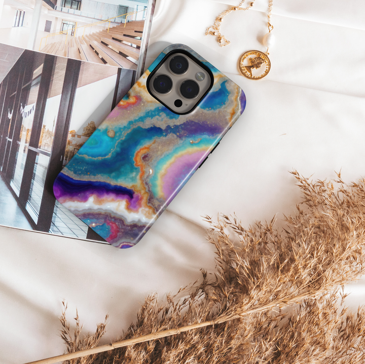Tough iPhone 16 MagSafe case featuring a colorful geode swirl pattern in turquoise, purple, gold, and white with a glossy finish.