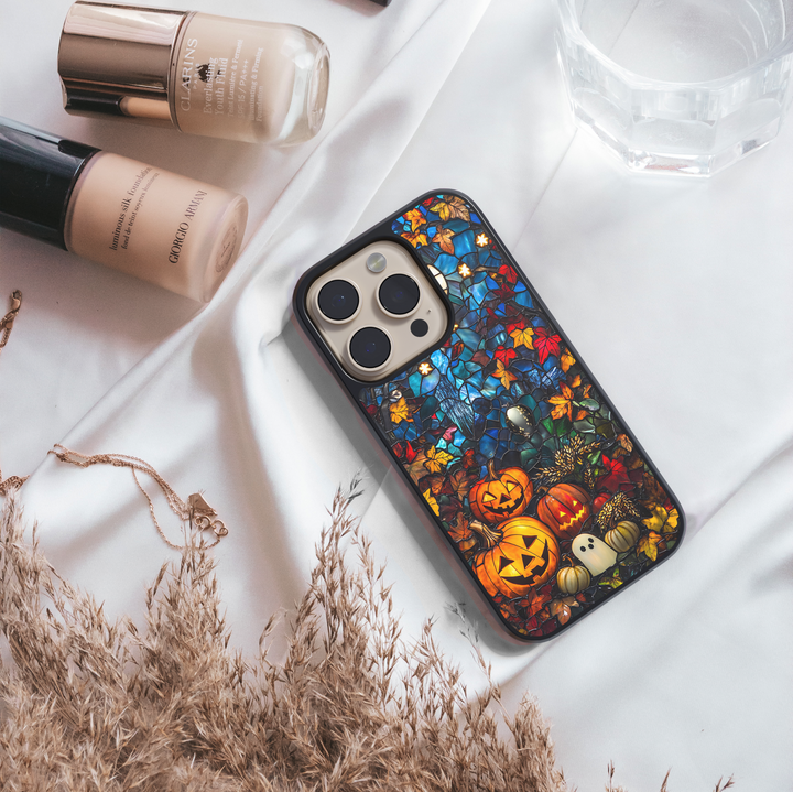 Halloween iPhone case with stained-glass style design, featuring glowing jack-o’-lantern pumpkins, ghost illustration, and colorful autumn leaves, protective fall aesthetic phone cover