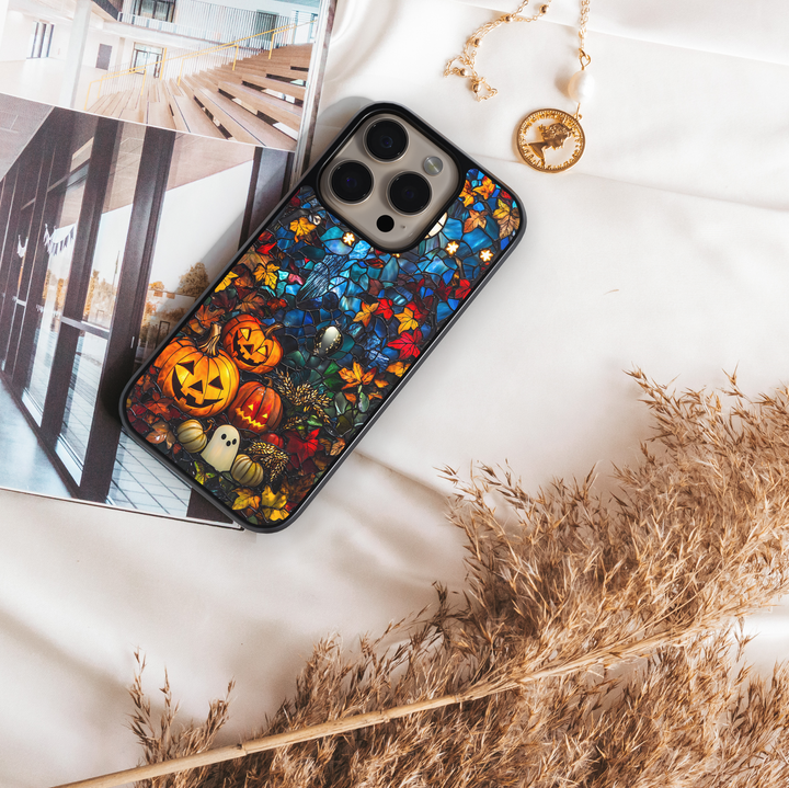 Halloween iPhone case with stained-glass style design, featuring glowing jack-o’-lantern pumpkins, ghost illustration, and colorful autumn leaves, protective fall aesthetic phone cover