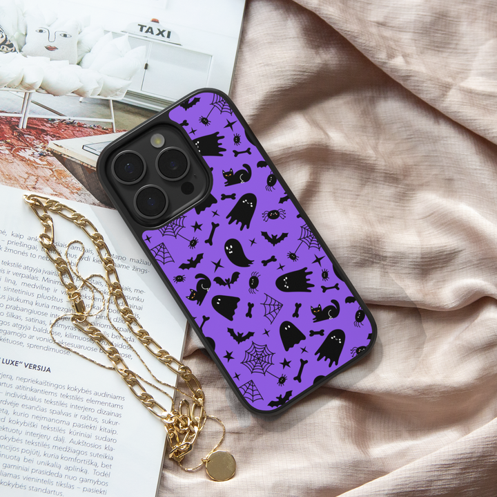 Purple phone case with cute black cats, spooky ghosts, bats, bones, and spider webs – Halloween aesthetic design for iPhone and Samsung.