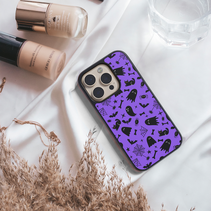 Purple phone case with cute black cats, spooky ghosts, bats, bones, and spider webs – Halloween aesthetic design for iPhone and Samsung.