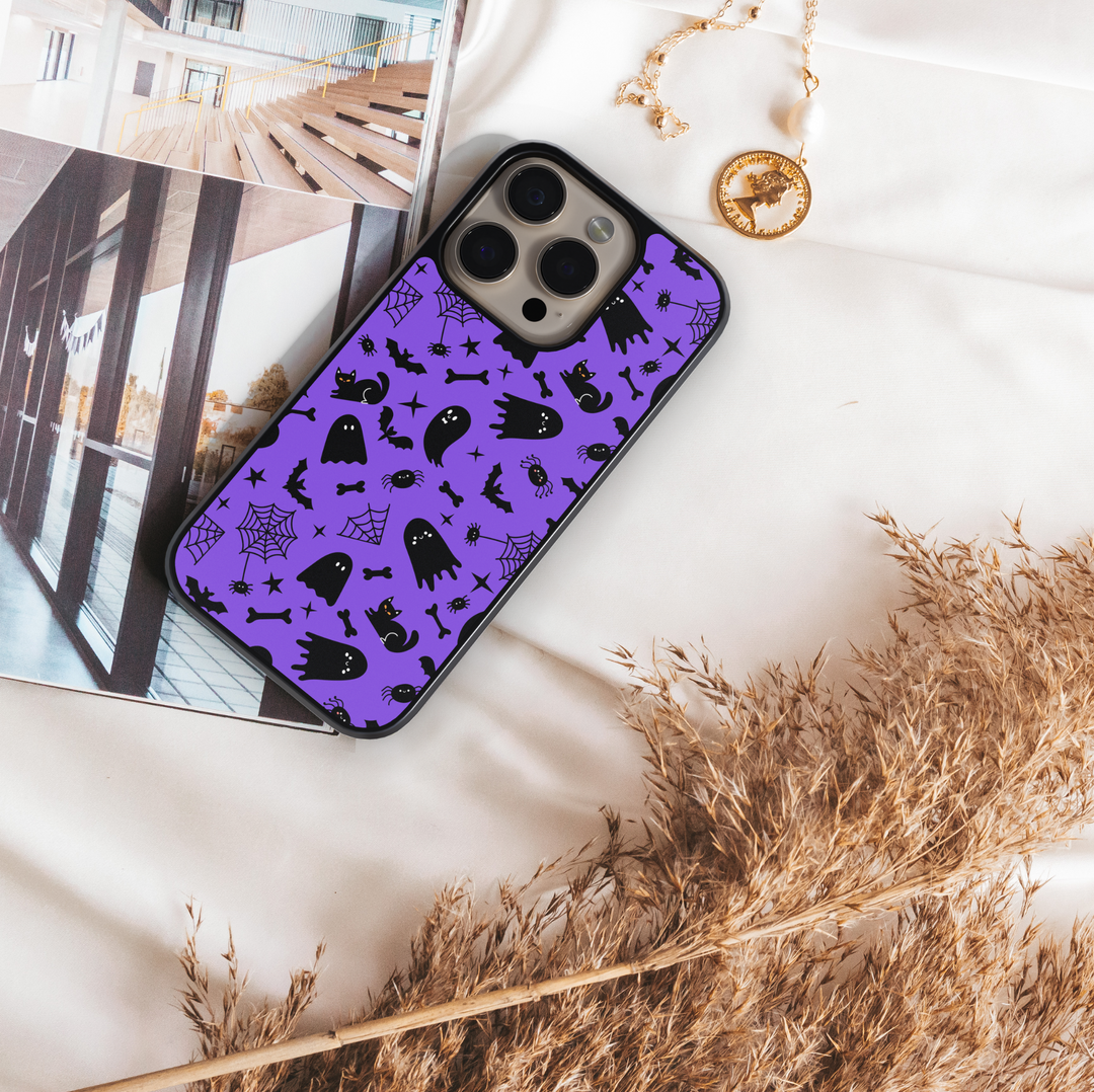 Purple phone case with cute black cats, spooky ghosts, bats, bones, and spider webs – Halloween aesthetic design for iPhone and Samsung.