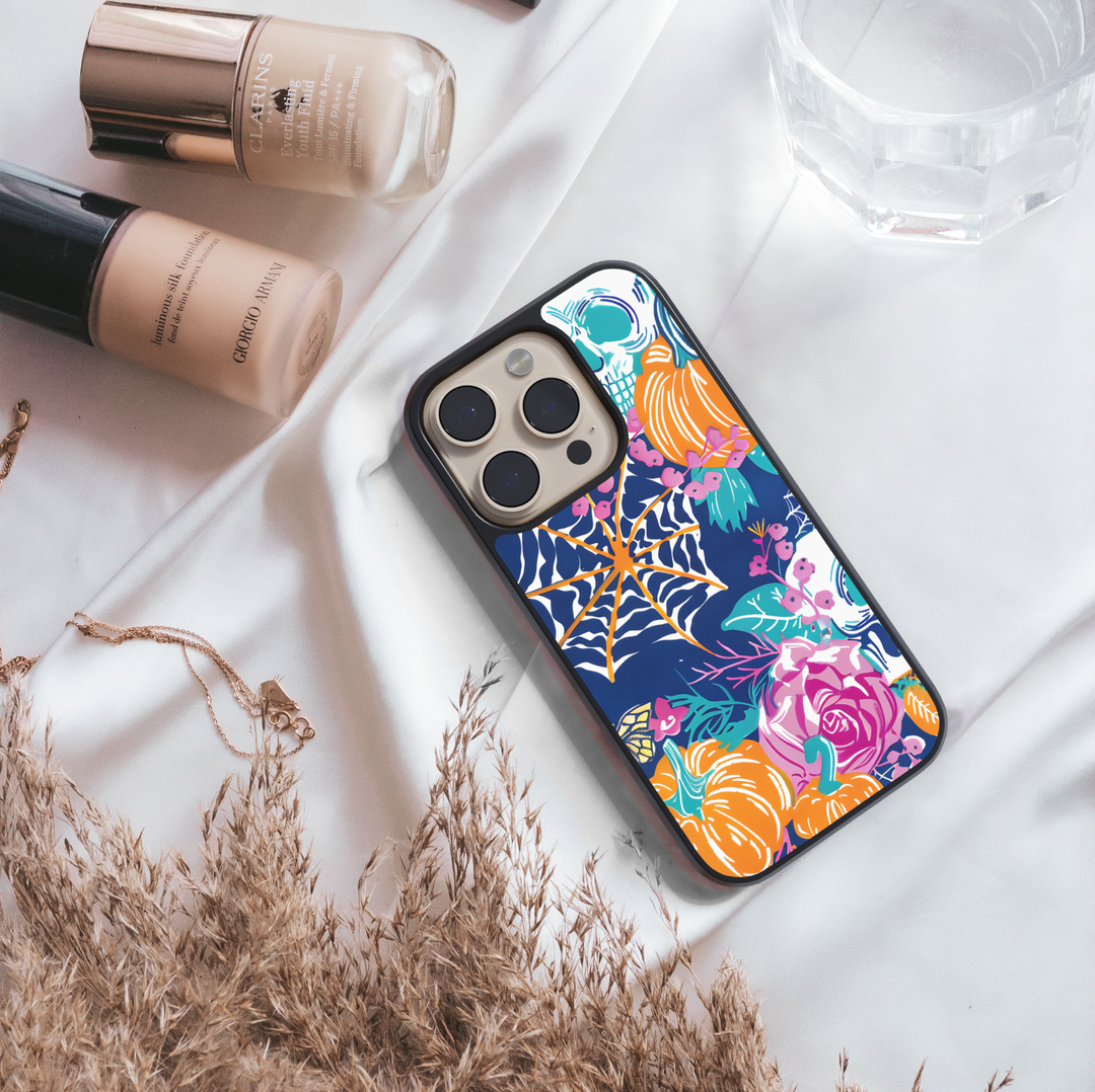 Midnight Bloom iPhone case with pumpkins, skull, spider web, and colorful floral design on navy background.