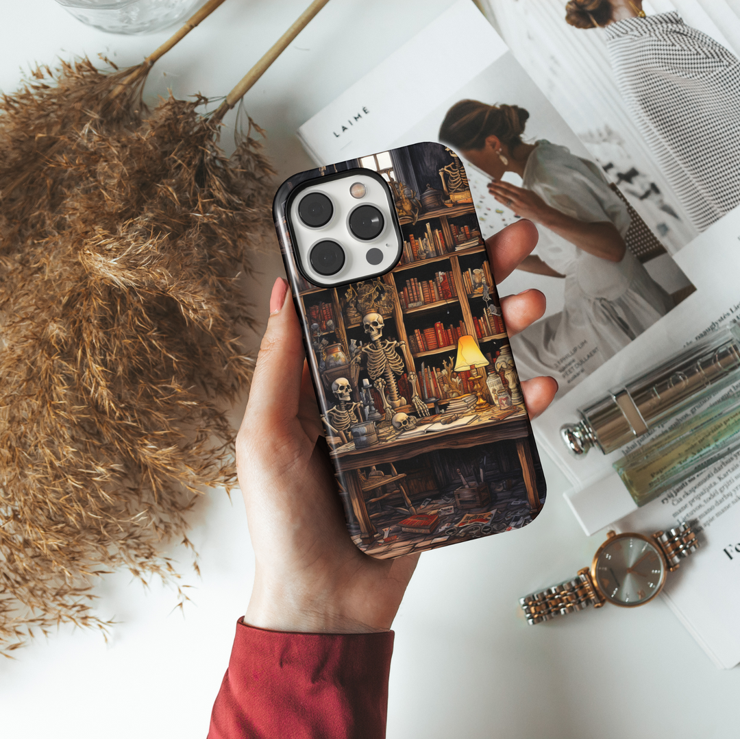 Skeleton iPhone case with a haunted library scene featuring skeletons, books, vintage desk, eerie lighting, skulls, and spooky Halloween elements.