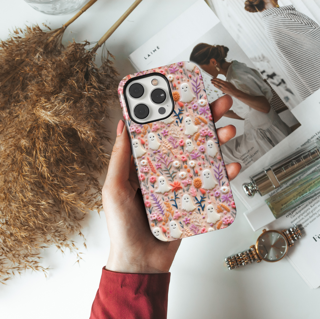 Cute Halloween ghost iPhone case with pastel pink, peach, and orange flowers on a soft background. Perfect spooky season aesthetic with smiling mini ghosts.