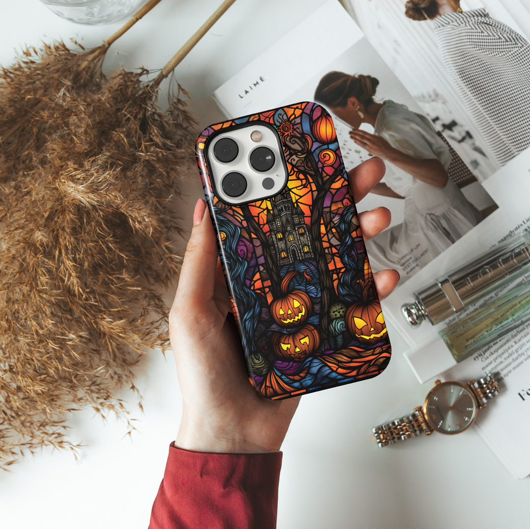 Stained glass Halloween iPhone case with glowing jack-o'-lanterns, spooky trees, and a haunted castle in vibrant orange, purple, and black tones.