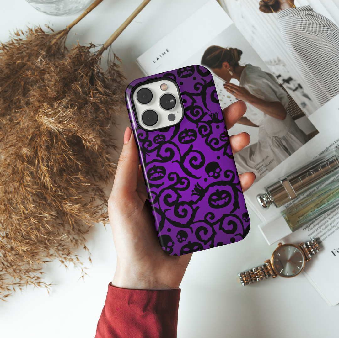 Purple iPhone case with swirling black Halloween vines, spooky jack-o'-lantern faces, skulls, and dark gothic pattern. Perfect for Halloween season aesthetic