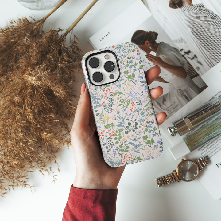 iPhone case featuring a delicate and colorful wildflower pattern with tiny blossoms and greenery on a soft cream background.