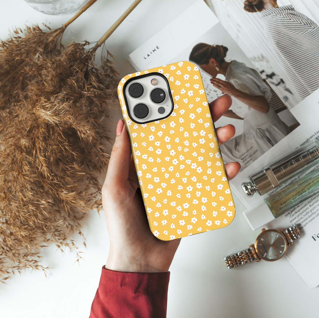 iPhone case featuring a playful mustard yellow background with a scattered pattern of tiny white and pink daisies.