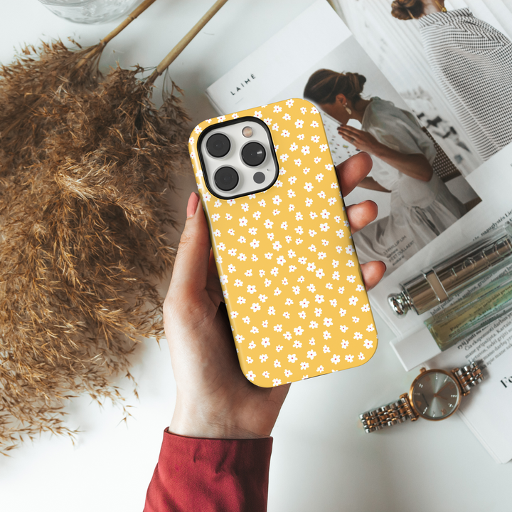 iPhone case featuring a playful mustard yellow background with a scattered pattern of tiny white and pink daisies.