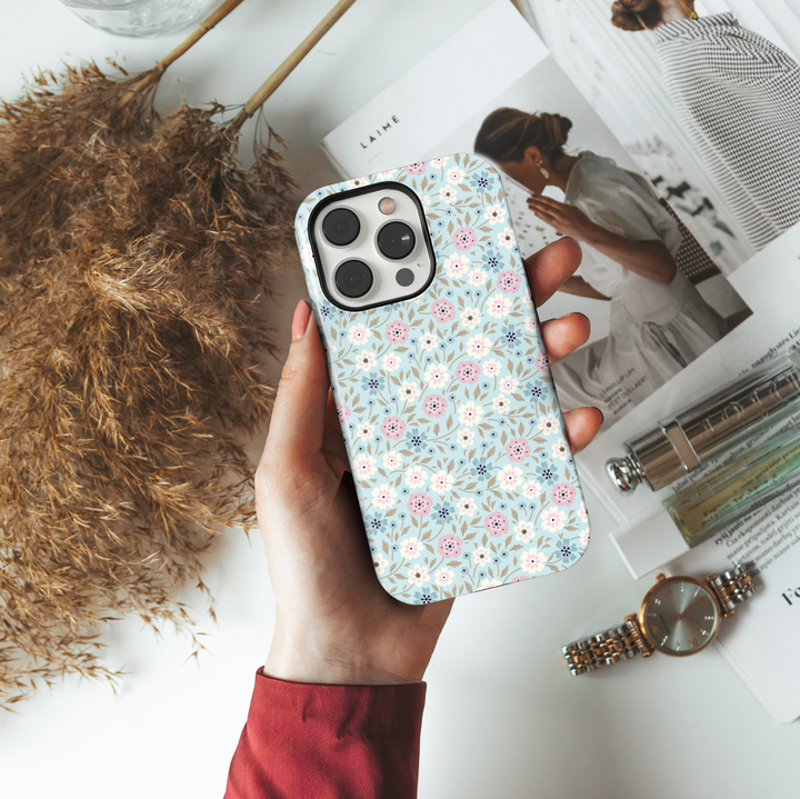 iPhone case with a pastel blue background and a dainty floral print in soft pink, white, navy, and taupe tones, creating a sweet and vintage-inspired look.