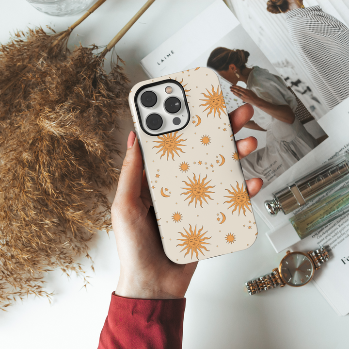 Cream celestial iPhone case with vintage orange sun faces, crescent moons, and scattered stars in a hand-drawn style.