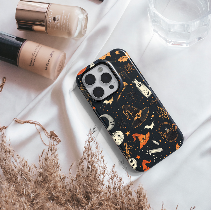 Black iPhone case with Halloween design featuring witch hats, bats, crescent moons, cobwebs, stars, and orange accents – protective and aesthetic tough cover.