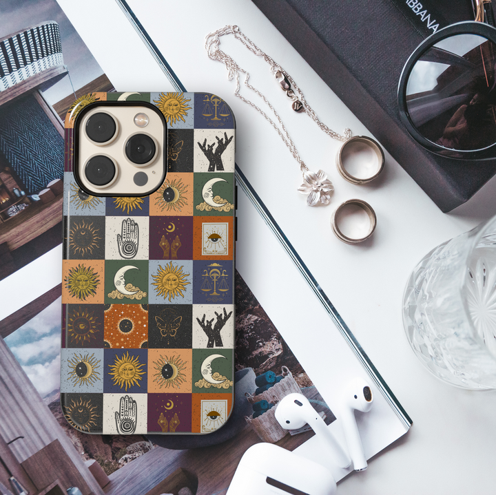Colorful checkerboard iPhone case featuring boho mystical symbols like suns, moons, butterflies, hands, scales, and eyes in warm and earthy tones.