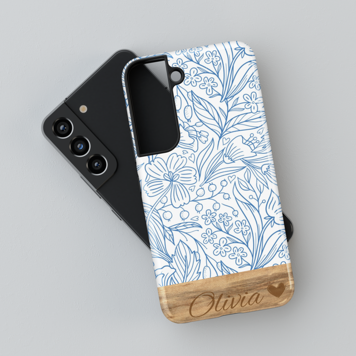 Elegant Samsung Galaxy phone case featuring a blue floral line art design with a woodgrain-textured bottom, personalized with a name engraving. Available for Samsung Galaxy S25 Ultra, S24 FE, S23, and more.