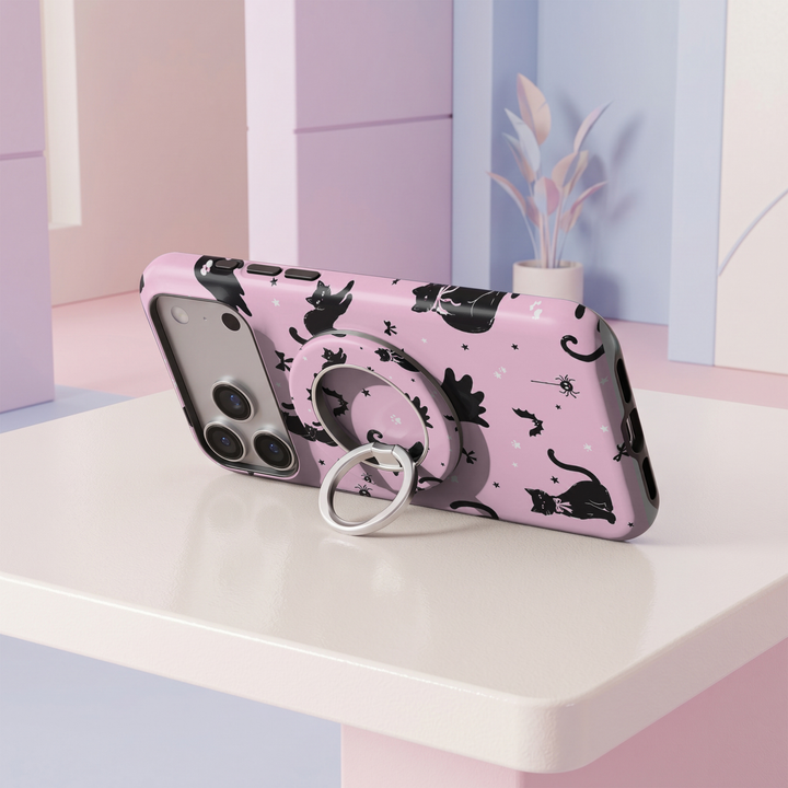 Pink Halloween MagSafe ring holder featuring playful black cats, tiny spiders, bows, stars, and a silver magnetic phone grip and stand.