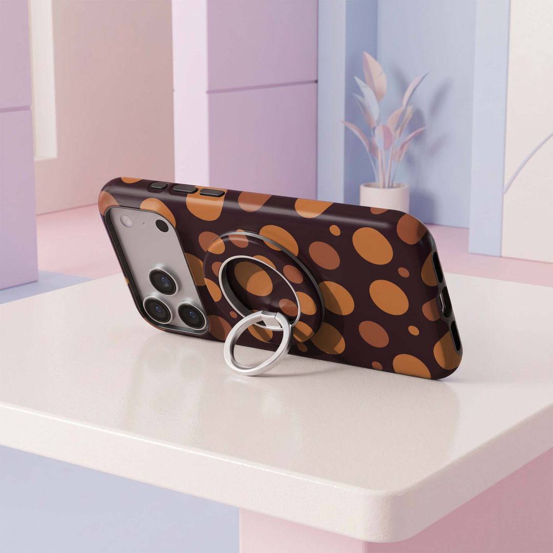 CASELIX Amber Dots MagSafe Ring Holder featuring oversized burnt orange and caramel polka dots on a deep chocolate burgundy background, with a silver rotating metal finger ring for a chic, retro-inspired phone accessory.
