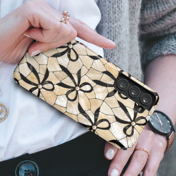 Elegant Samsung Galaxy S26 Ultra case with black bows and pearl details on an ivory mosaic background.