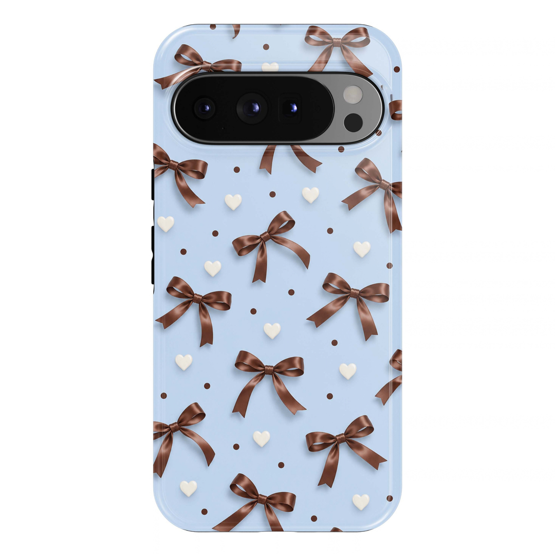 Cocoa Bows Google Pixel case featuring chocolate brown satin ribbon bows, ivory hearts and small brown polka dots against a soft powder blue background.