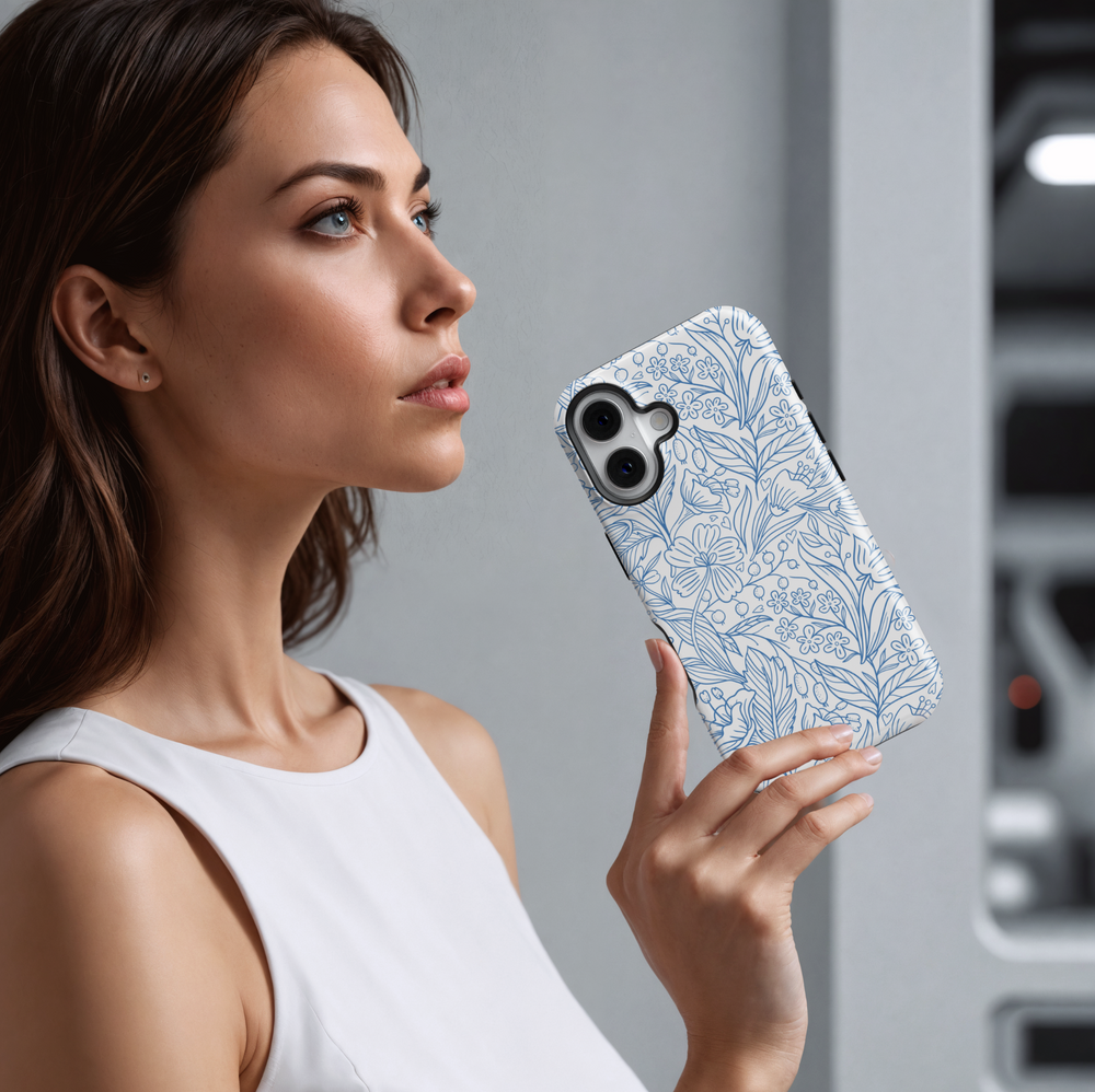 White iPhone case featuring a detailed blue floral line art pattern with various wildflowers, leaves, and berries, creating a clean and elegant botanical look.