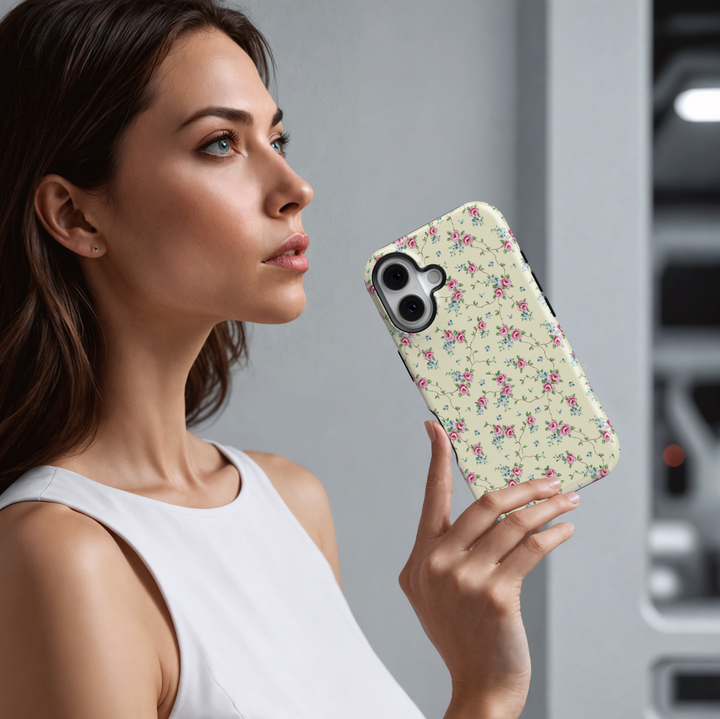 Cream iPhone case adorned with a vintage-inspired pattern of delicate pink roses and tiny blue florals connected by thin trailing vines, creating a romantic, timeless aesthetic.