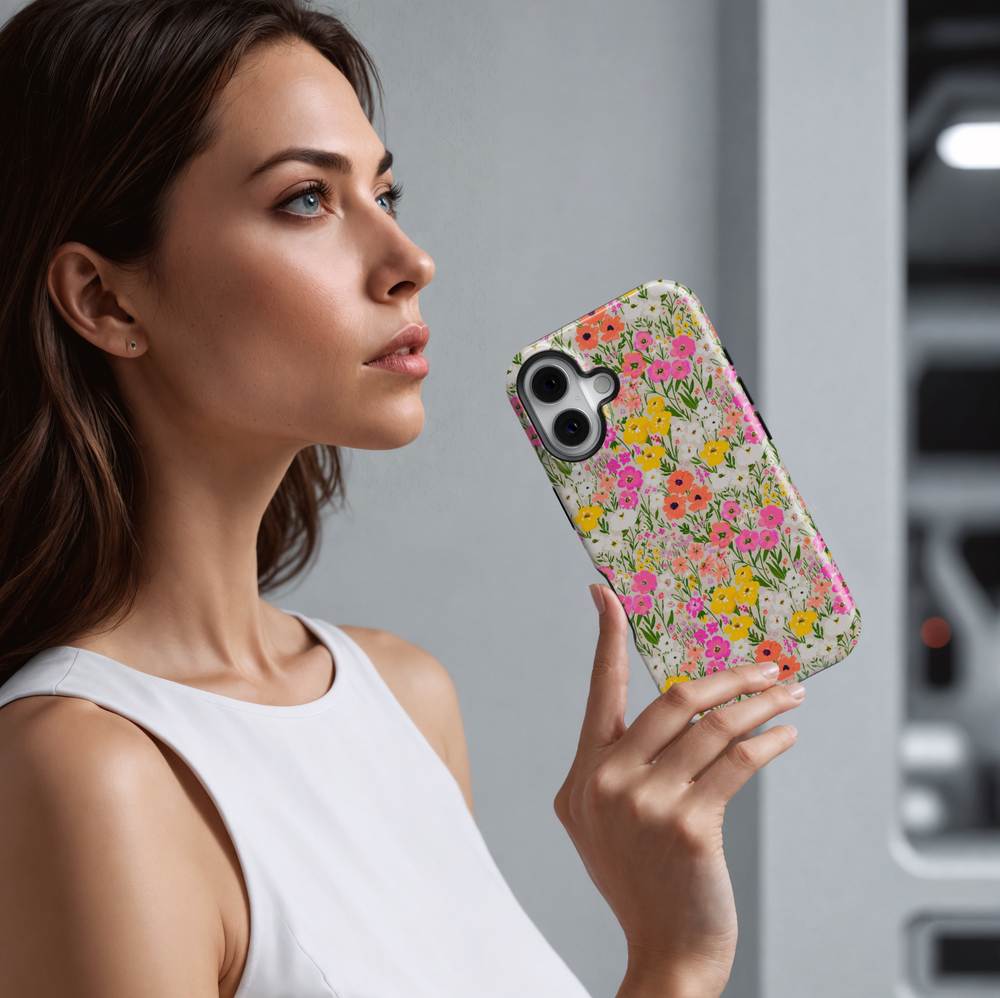 Charming iPhone case with a vibrant wildflower meadow pattern featuring hand-painted flowers in pink, yellow, coral, and white on a soft cream background.
