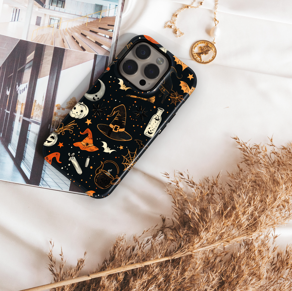 Black iPhone case with Halloween design featuring witch hats, bats, crescent moons, cobwebs, stars, and orange accents – protective and aesthetic tough cover.