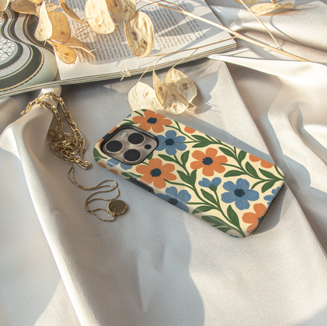 Vintage floral iPhone case featuring blue and orange hand-painted flowers with green leaves on a cream background.