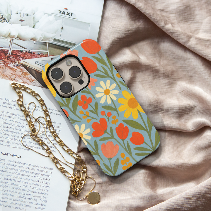 Retro floral iPhone case featuring colorful daisies, tulips, and wildflowers on a soft blue background with vintage folk art styling.