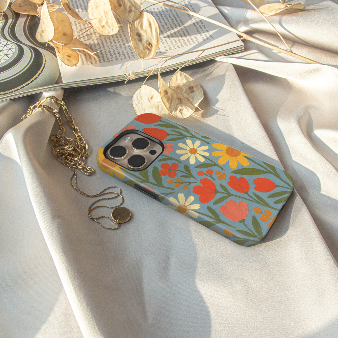 Retro floral iPhone case featuring colorful daisies, tulips, and wildflowers on a soft blue background with vintage folk art styling.