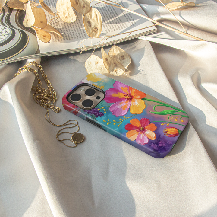 Colorful floral iPhone case featuring vibrant hand-painted flowers in pink, orange, yellow, and purple with a bright botanical garden design.