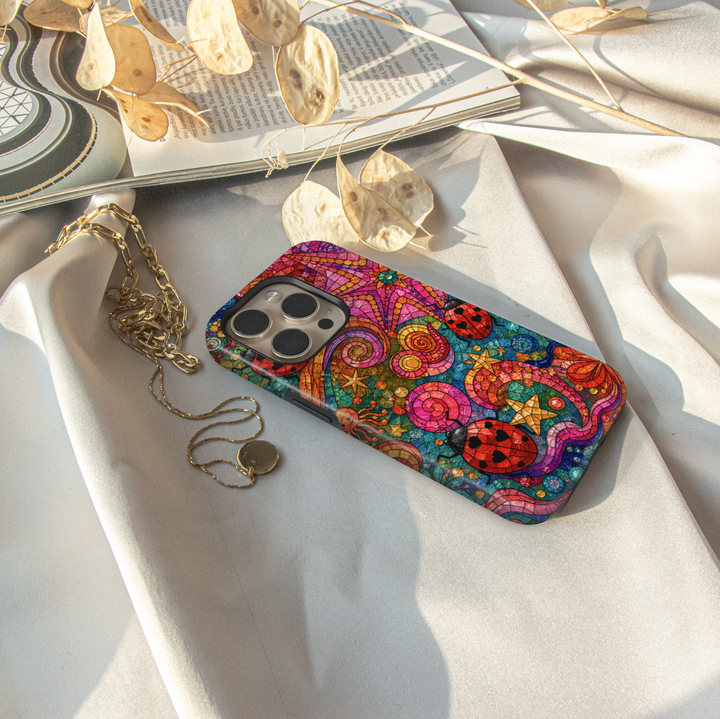 Colorful stained glass iPhone case featuring ladybugs, swirling patterns, stars, and whimsical mosaic artwork.