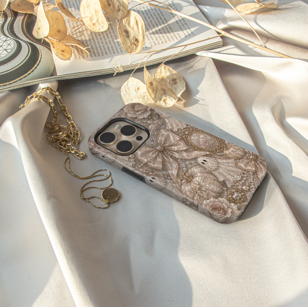 Elegant Ghost Coquette iPhone case featuring pearl ghost, satin bows, ivory pumpkins, vintage mirror, pearls, lace, and neutral Halloween décor.