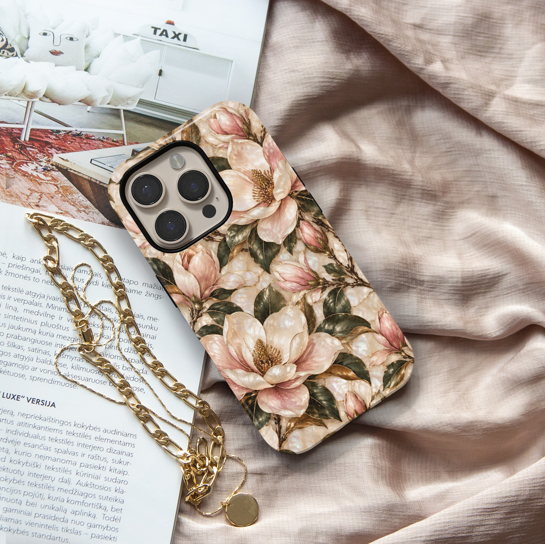 January birth flower iPhone 18 Pro Max case featuring Magnolia Grace with elegant ivory and blush pink magnolia blossoms, golden botanical accents, and deep green leaves on a champagne-inspired background with a glossy printed finish.