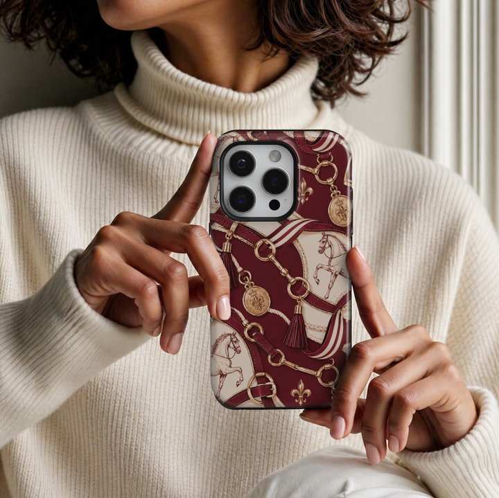 CASELIX Equestrian Elegance iPhone 18 Pro Max case featuring a luxurious burgundy and cream equestrian print with vintage horse illustrations, gold horsebit hardware, leather riding straps, decorative tassels, striped ribbons, and gold medallions in a glossy printed finish.
