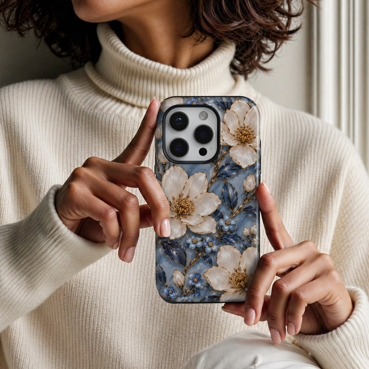 CASELIX Sapphire Blossom iPhone case featuring elegant ivory white flowers, delicate sapphire blue blossoms, navy blue leaves and intricate gold detailing against a soft blue marble-inspired background with a glossy printed finish.