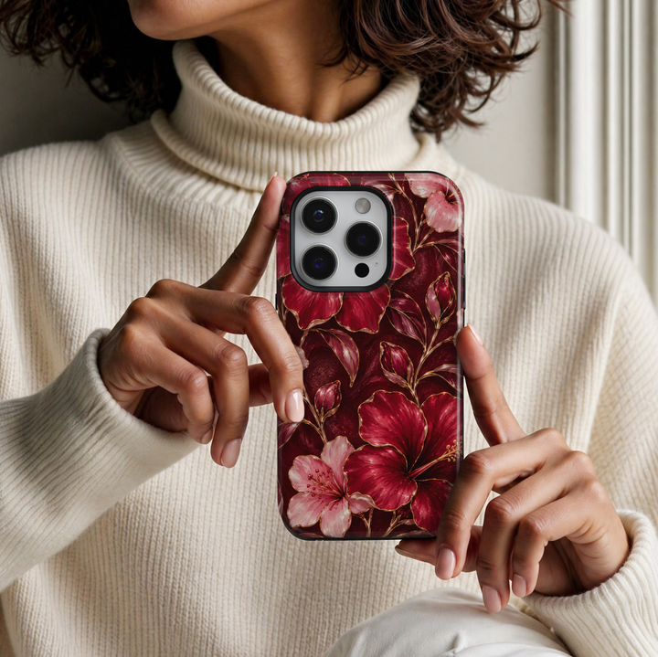CASELIX Ruby Hibiscus iPhone case featuring vibrant ruby red and blush pink hibiscus flowers with delicate gold outlines, floral buds and a deep burgundy background in a glossy printed finish.