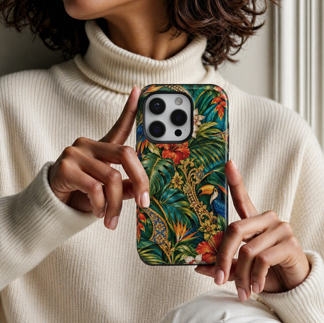 CASELIX Tropical Paradise Luxe iPhone Tough MagSafe protective phone case featuring a luxurious tropical rainforest design with vibrant hibiscus flowers, exotic birds, lush emerald-green foliage, and ornate golden botanical accents. The captivating artwork showcases a magnificent blue toucan with brilliant sapphire feathers, a striking golden-orange beak, and delicate white facial markings, perched among richly layered tropical leaves. Oversized scarlet-red and fiery coral hibiscus blossoms bloom alongside 