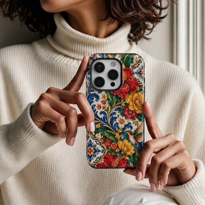 CASELIX Mediterranean Hummingbird Garden iPhone Tough MagSafe protective phone case featuring a vibrant Mediterranean-inspired floral design with an elegant multicolored hummingbird, brilliant red hibiscus blossoms, golden-yellow flowers, lush emerald-green foliage, and intricate cobalt-blue ornamental scrollwork. The luxurious artwork showcases a beautifully detailed hummingbird in flight with shimmering emerald-green, turquoise-blue, ruby-red, and golden feathers, gracefully hovering among richly layered 