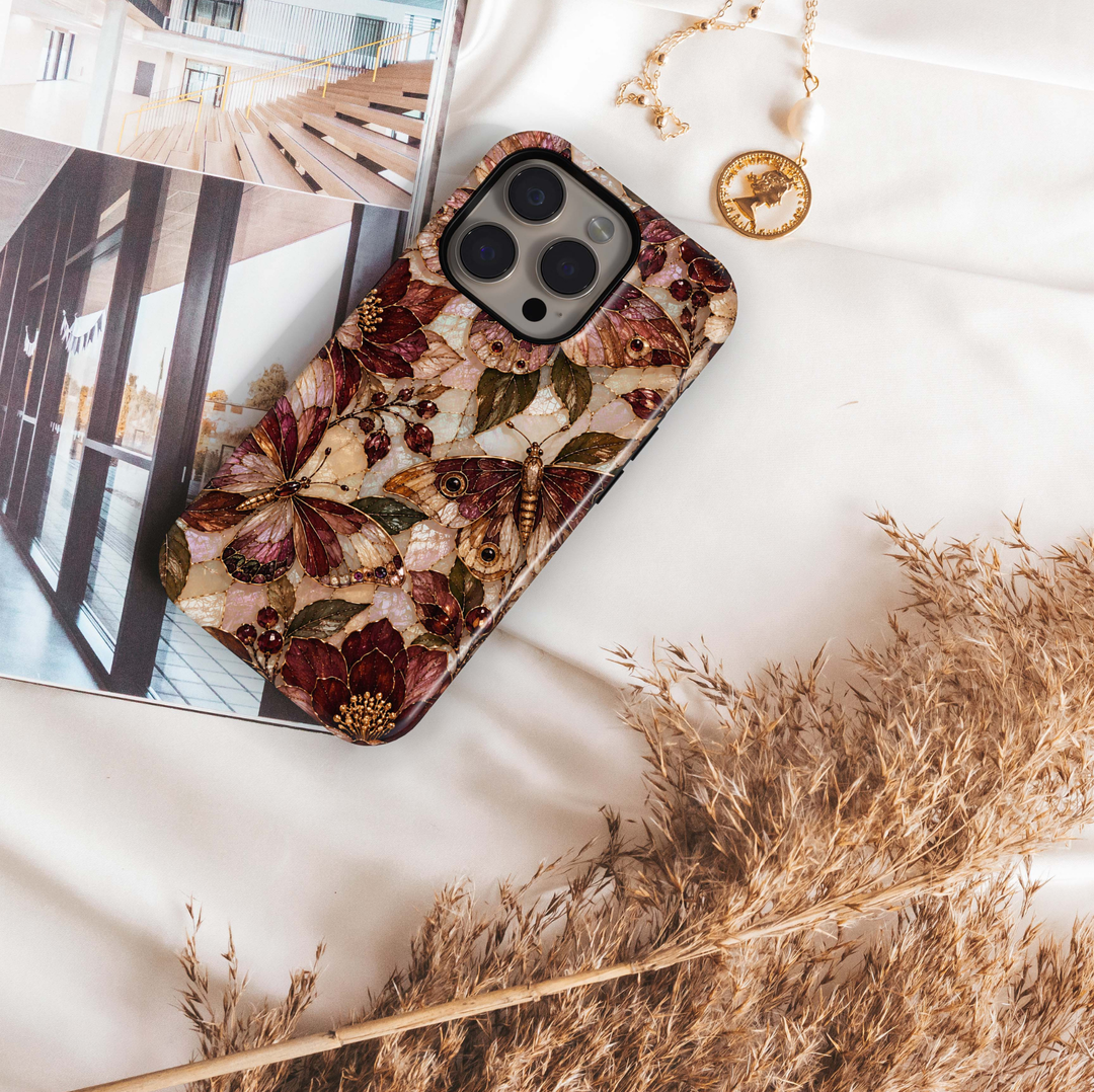Cabernet Butterfly iPhone 18 Pro Max MagSafe case featuring stained-glass-inspired butterflies and moths in cabernet, burgundy, champagne and bronze with olive foliage and jewel-like berries over a pearlescent background, a luxurious tough iPhone 18 Pro butterfly phone case with MagSafe compatibility.