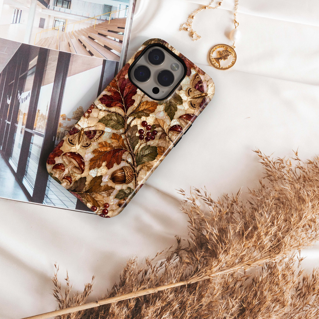 Enchanted Acorn iPhone 18 Pro Max MagSafe case featuring acorns, woodland mushrooms, moths, red berries and autumn leaves in chestnut, burgundy, amber and olive over a pearlescent stained-glass background, a whimsical tough iPhone 18 Pro fall phone case with MagSafe compatibility.
