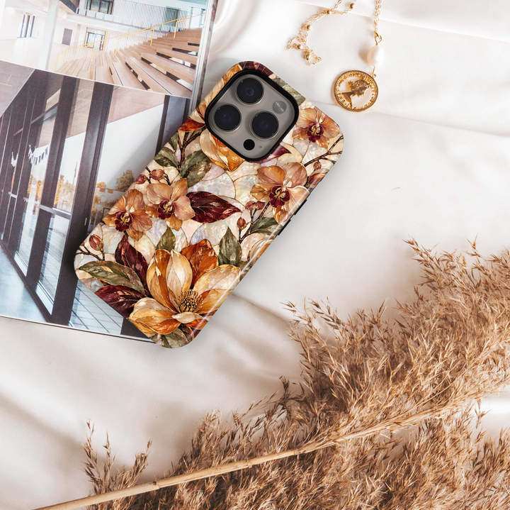 Amber Orchid iPhone 18 Pro Max MagSafe case featuring pearlescent orchids and botanical blooms in amber, champagne, caramel and ivory with burgundy and olive leaves, a luxurious stained-glass-inspired tough iPhone 18 Pro floral phone case with MagSafe compatibility.