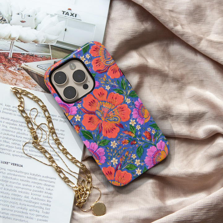 Electric Bloom iPhone case featuring vibrant coral, pink and orange flowers with green leaves on a cobalt blue background.