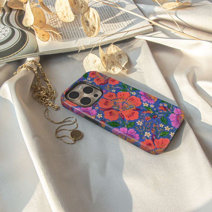 Electric Bloom iPhone case featuring vibrant coral, pink and orange flowers with green leaves on a cobalt blue background.