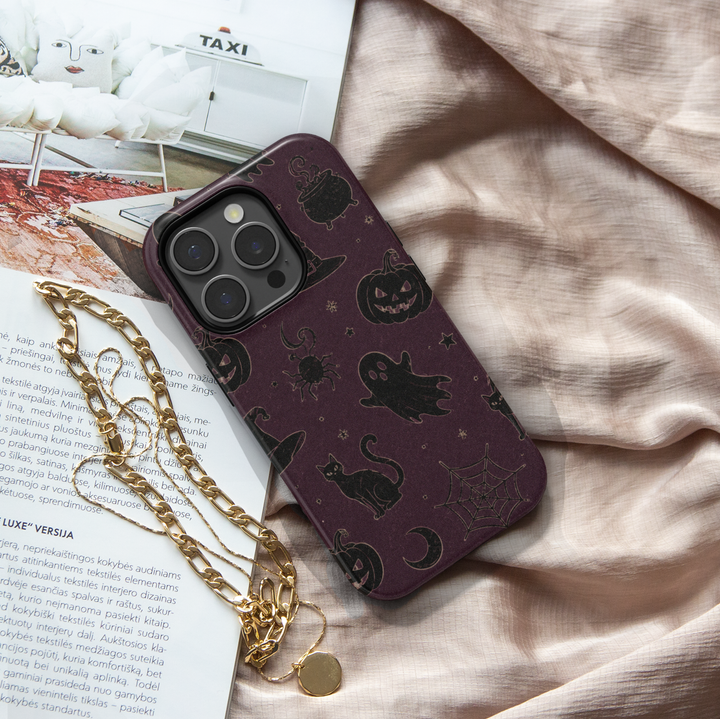 Midnight Witchery iPhone case with black cats, ghosts, pumpkins, witch hats, cauldrons, spiders and moons on a dark plum Halloween background.