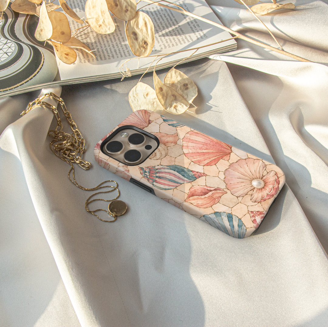 Pastel seashell iPhone case featuring pink scallop shells, spiral shells, pearl accents, and a soft coastal beach design.