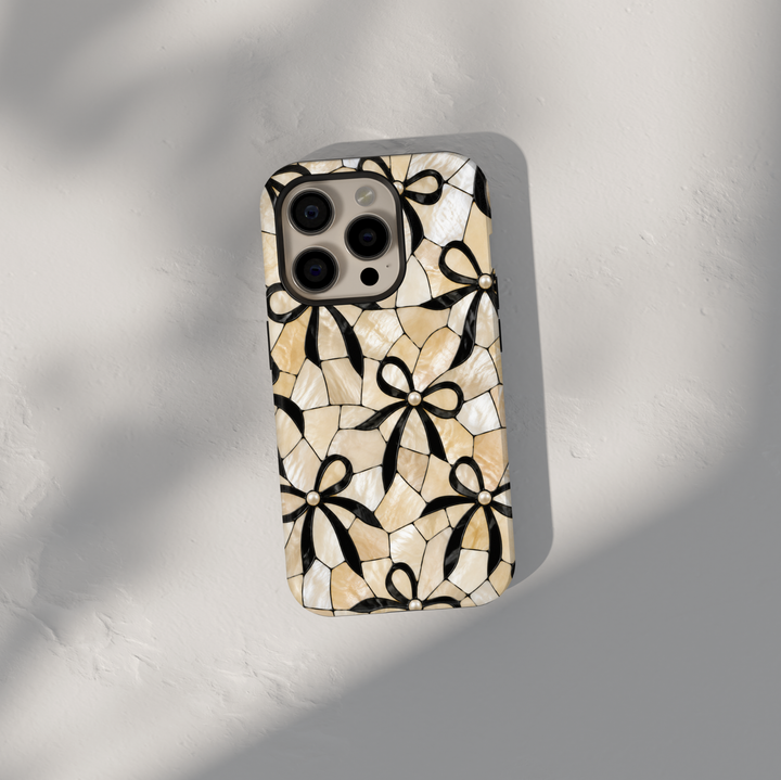 Ivory mosaic iPhone 17 Pro Max case with black bow pattern and pearl accents in a classy aesthetic design.